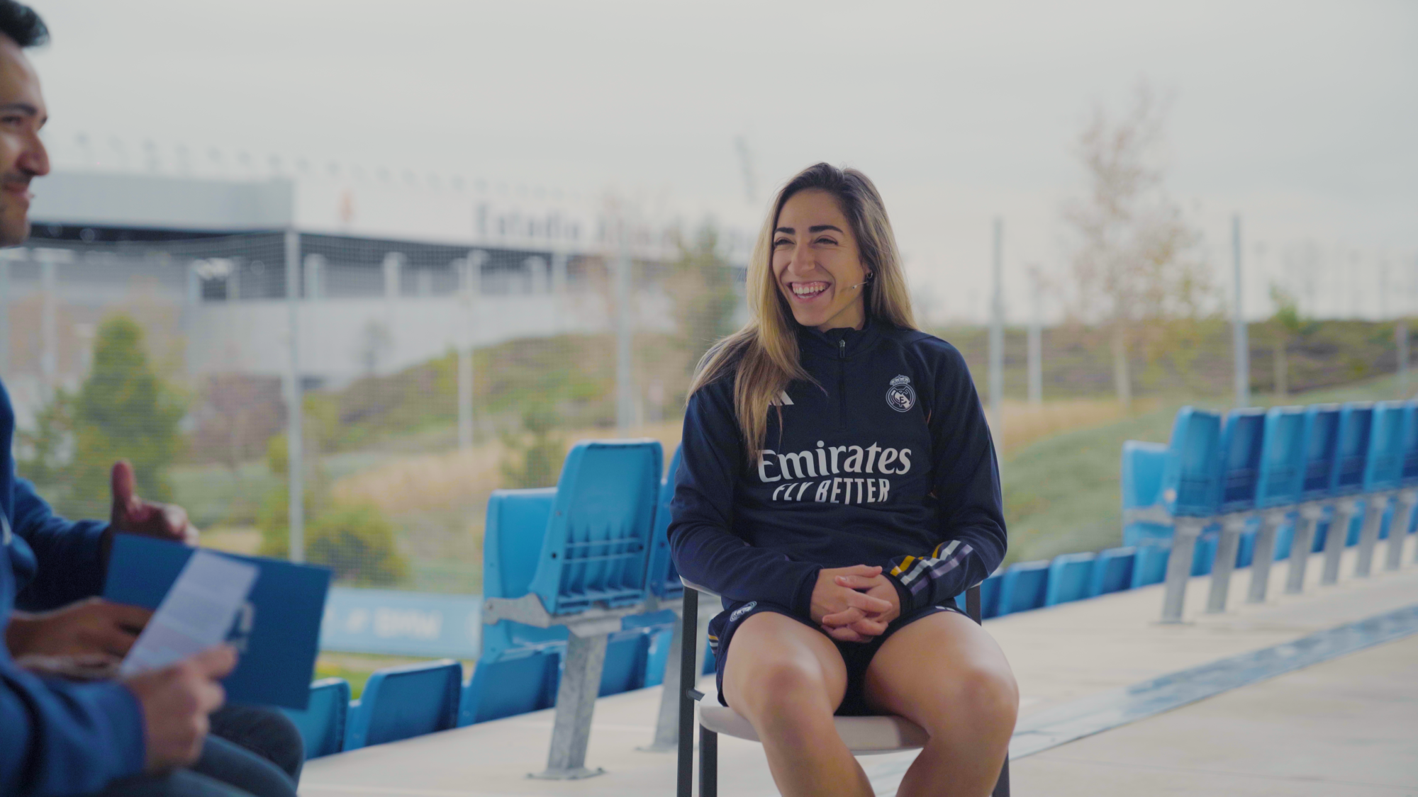 Olga Carmona jugadora del Real Madrid riendo en una entrevista para madridistaReal y de fondo el estadio Di Estefano